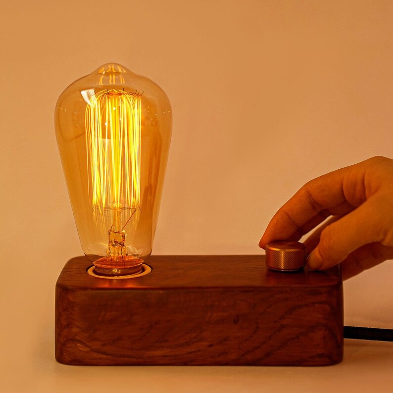 May include: A wooden table lamp with a vintage-style light bulb and a brass switch. The lamp is switched on and the light bulb is glowing.