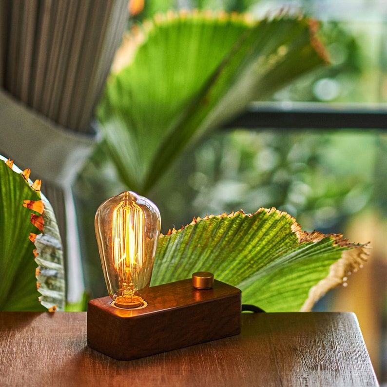 May include: A wooden table lamp with a vintage-style light bulb. The lamp has a dark brown wooden base and a brass switch. The light bulb is on and glowing.