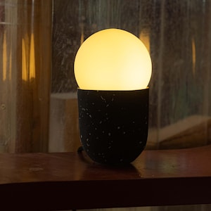 May include: A black and white speckled table lamp with a round, white, light bulb.