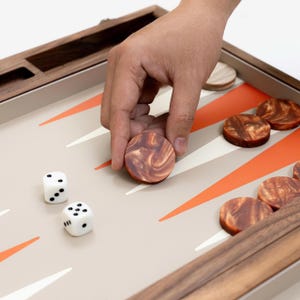 May include: A backgammon set with a wooden frame and playing pieces. The game board is beige with orange and white triangles. The wooden game pieces have a marbled appearance. Two white dice are also visible.