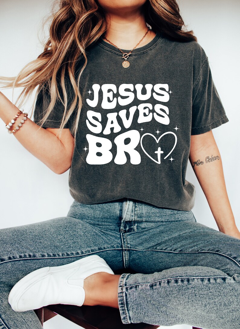 May include: A dark gray t-shirt with the text "JESUS SAVES BRO" in white with a heart and cross graphic.
