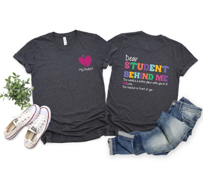 May include: Two dark gray t-shirts with a teacher-themed design. The front shirt has a pink heart with the text "My Student". The back shirt has the text "Dear Student Behind Me. The world is a better place with you in it. Love, The teacher in front of you." in rainbow colors.