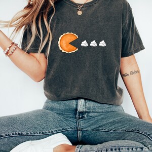 Peut inclure: T-shirt gris fonc&eacute; avec un motif en forme de tarte, avec une part manquante, suivi de trois boules de cr&egrave;me fouett&eacute;e blanches. Le t-shirt est de style d&eacute;contract&eacute;, adapt&eacute; au quotidien.