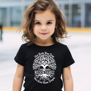 May include: A black t-shirt with a white tree design. The tree has a heart in the center with the year 2023 inside. The text "Our Roots Run Deep" is above the tree, "Family Reunion" is below the tree, and "WILSON FAMILY" is in the center of the tree. The text "Our Love Runs Deeper" is below the roots.