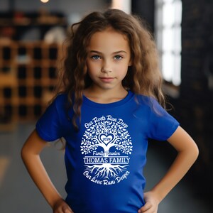 May include: A blue t-shirt with a white tree design. The tree has a heart in the center with the year 2024 inside. The text "Our Roots Run Deep" is above the tree, and the text "Our Love Runs Deeper" is below the tree. The text "Family Reunion THOMAS FAMILY" is in the center of the tree.