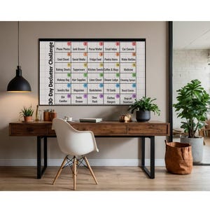 May include: A 30-Day Declutter Challenge calendar in a black frame hangs above a wooden desk. The calendar is a grid with numbered boxes, each listing an item to declutter. The desk has a white chair, plants, and a black lamp.