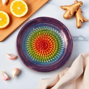 Peut inclure: Un presse-ail en céramique colorée avec un motif arc-en-ciel. Le presse-ail est entouré de gousses d'ail, de moitiés de citron et de racine de gingembre. Le presse-ail a une surface texturée pour un râpage facile. C'est un ustensile de cuisine.