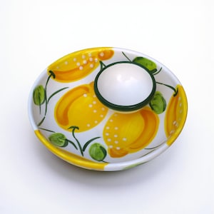 Puede incluir: Plato de cerámica ovalado con un cuenco central para salsas. El plato es blanco con un diseño de limones amarillos y verdes. El cuenco es blanco con un borde verde. El borde del plato es amarillo.