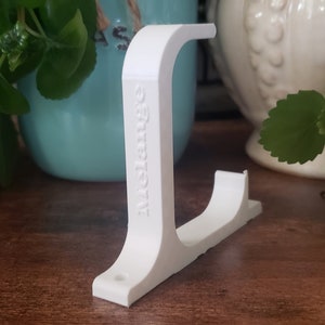 May include: White plastic wall mount with the word "Controller" printed on the side. The mount is designed to hold a video game controller.