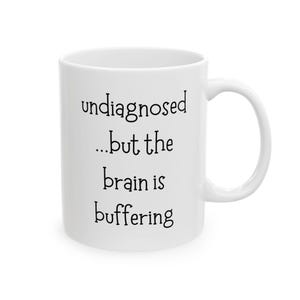 May include: White ceramic mug with the text "undiagnosed...but the brain is buffering" in black, sans-serif font. The mug has a curved handle and a glossy finish. A humorous and relatable item.