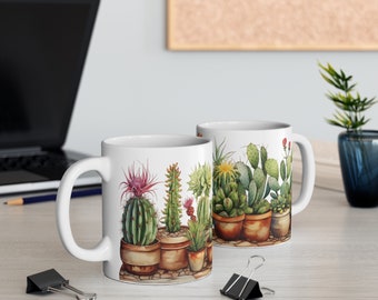 May include: Two white ceramic mugs with a watercolor illustration of various cacti in terracotta pots. The cacti feature green, pink, and yellow hues. The mugs are on a light-colored wooden surface.