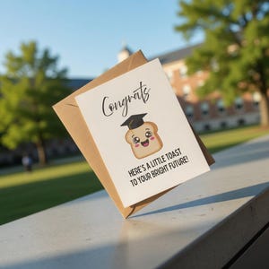 Puede incluir: Tarjeta de felicitación de graduación con un personaje de tostada de dibujos animados con birrete. La tarjeta dice "¡Enhorabuena!" y "¡Aquí tienes un brindis por tu brillante futuro!" con un sobre marrón.