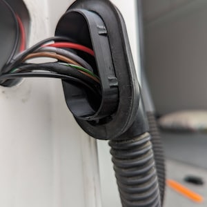 Op de afbeelding: Close-up van een zwarte rubberen doorvoer met meerdere draden die erdoorheen lopen. De draden zijn rood, bruin, groen en zwart.
