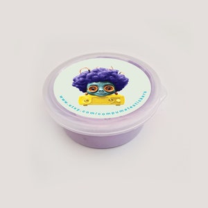 May include: A small, round, clear plastic container with a light purple substance inside. The lid features a circular sticker with a cartoon character with purple hair and orange eyes. The sticker also includes the text "www.etsy.com/compumatestickers".