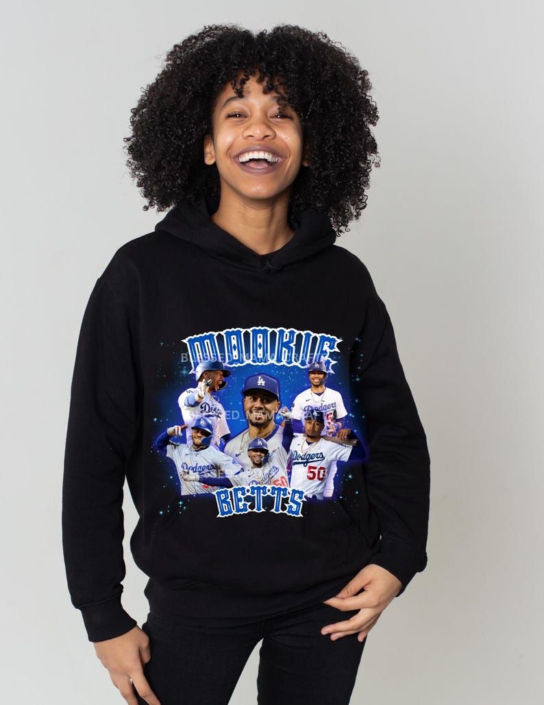 May include: Black hoodie featuring a graphic print of baseball players in blue and white uniforms with the text "Mookie Betts" in blue and white. The background is a blue and purple gradient with stars.