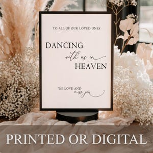 May include: A rectangular black frame containing a white sign with black text that reads: TO ALL OF OUR LOVED ONES DANCING with us in HEAVEN WE LOVE AND miss you. The sign is mounted on a circular black base and features elegant typography.