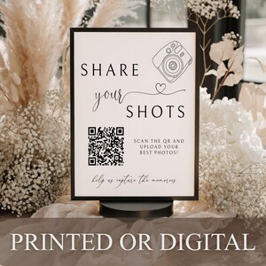 May include: A rectangular sign in a black frame featuring the text SHARE your SHOTS, a line drawing of a camera, a heart icon, a QR code, and the text SCAN THE QR AND UPLOAD YOUR BEST PHOTOS! with help us capture the memories at the bottom.