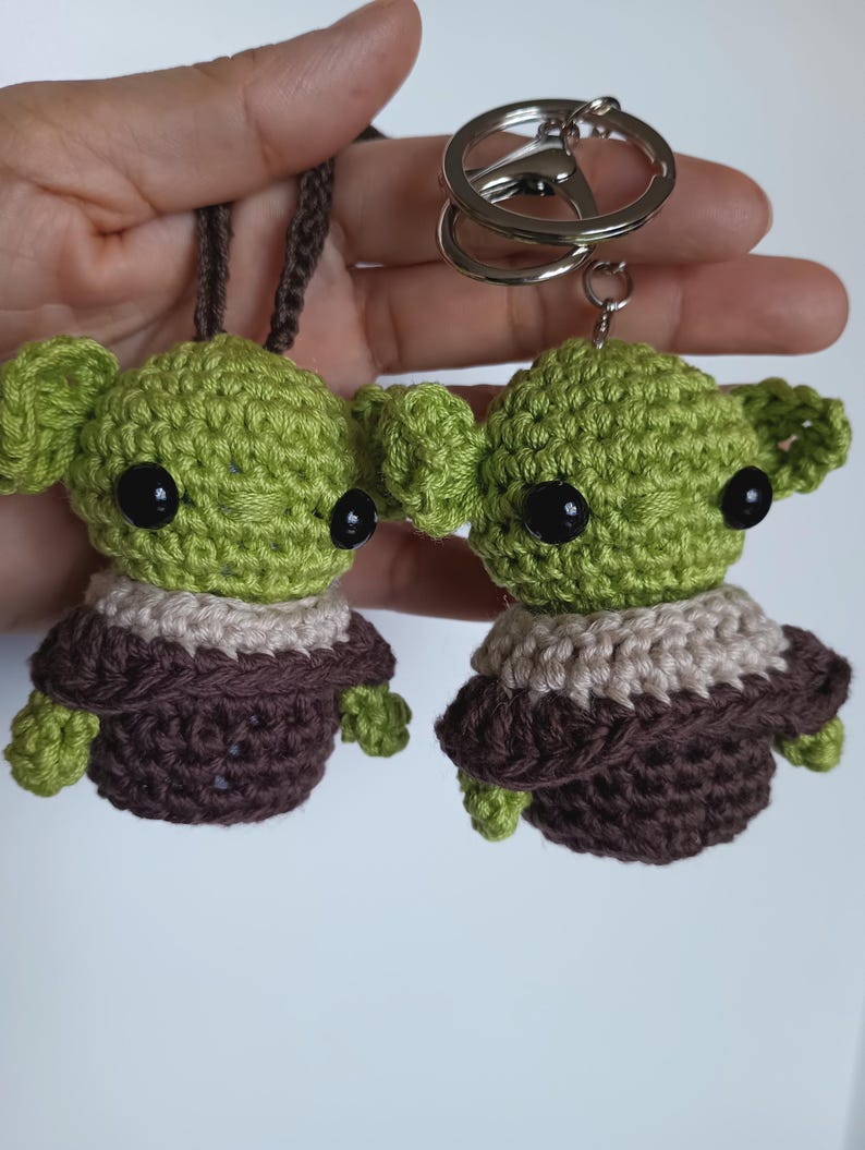 Puede incluir: Dos figuras de extraterrestres verdes de ganchillo con ojos negros y t&uacute;nicas marrones. Una est&aacute; unida a un cord&oacute;n marr&oacute;n, la otra a un llavero plateado. Las figuras tienen orejas grandes y est&aacute;n hechas a mano.