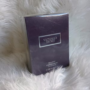 May include: A rectangular, dark purple box of Victoria's Secret Basic Instinct Eau de Parfum. The box has a silver label with the brand name and product name. The bottle contains 100 ml / 3.4 fl oz of perfume.