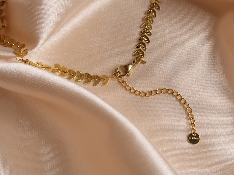 Puede incluir: Un collar de cadena dorada con un delicado dise&ntilde;o de hojas. La cadena tiene un cierre de langosta y una cadena extensora con un peque&ntilde;o dije que dice "S. Alex".