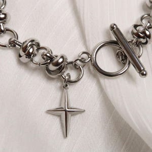 Puede incluir: Un brazalete de cadena de plata con un dije de estrella y un cierre de palanca. La cadena est&aacute; hecha de c&iacute;rculos unidos con un dise&ntilde;o de nudo.