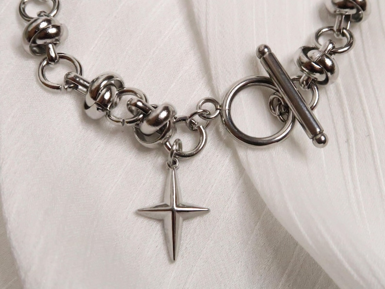 Puede incluir: Un brazalete de cadena de plata con un dije de estrella y un cierre de palanca. La cadena est&aacute; hecha de c&iacute;rculos unidos con un dise&ntilde;o de nudo.