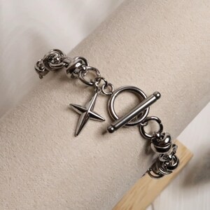 Puede incluir: Un brazalete de plata con cierre de palanca y un dije de estrella. El brazalete est&aacute; hecho de una cadena gruesa y robusta.