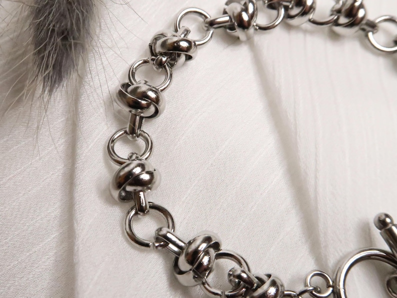 Puede incluir: Un brazalete de cadena de plata con un dise&ntilde;o anudado. El brazalete tiene un cierre de broche.