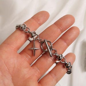 Puede incluir: Un brazalete plateado con cierre de palanca y un dije de estrella. El brazalete est&aacute; hecho de metal y tiene un dise&ntilde;o de cadena gruesa.