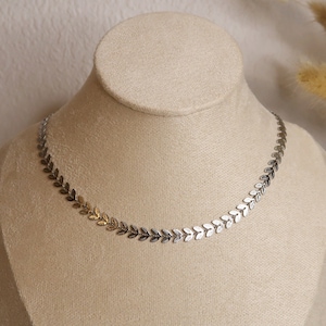 Puede incluir: Un collar de cadena de hojas plateadas y doradas en un expositor. El collar est&aacute; hecho de peque&ntilde;as hojas delicadas que est&aacute;n unidas entre s&iacute;.