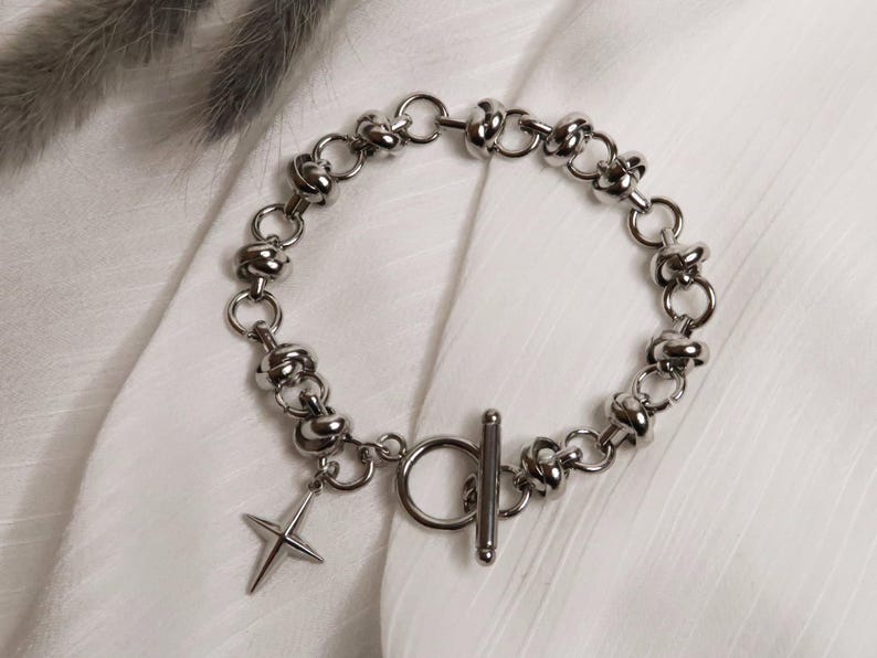 Puede incluir: Un brazalete de cadena de plata con un dije de estrella de plata y un cierre de palanca.