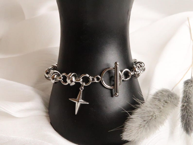 Puede incluir: Un brazalete de cadena de plata con un dije de estrella y un cierre de palanca.