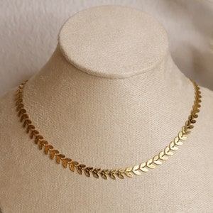 Puede incluir: Un collar de oro con una cadena delicada y peque&ntilde;os colgantes en forma de hoja. El collar se muestra en un maniqu&iacute; blanco.