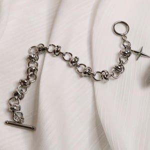 Puede incluir: Un brazalete de cadena de plata con un dije de estrella de plata. La cadena est&aacute; hecha de c&iacute;rculos unidos con un dise&ntilde;o de nudo.