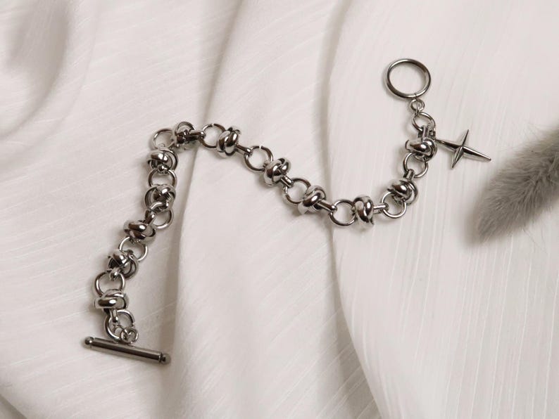 Puede incluir: Un brazalete de cadena de plata con un dije de estrella de plata. La cadena est&aacute; hecha de c&iacute;rculos unidos con un dise&ntilde;o de nudo.