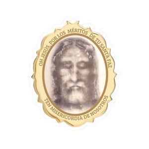 May include: A gold-coloured sticker with an oval shape and a scalloped edge. The sticker features a sepia-toned image of a face and text in Spanish. The text reads "OH JESUS, POR LOS MERITOS DE TU SANTA FAZ TEN MISERICORDIA DE NOSOTROS."