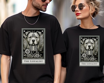 May include: Black t-shirts featuring a graphic of a dog with a skeleton design and the text "THE LOYALIST". The dog graphic is in a rectangular frame with stars. The shirts are worn by two people.