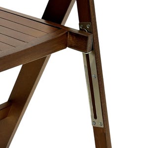 May include: Close-up of a wooden folding chair with a metal hinge and support. The chair is made of dark brown wood and has a slatted seat.