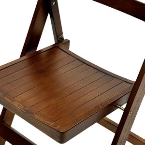 May include: A dark brown wooden folding chair with a slatted seat and a simple design. The chair is made of solid wood and has a sturdy construction.