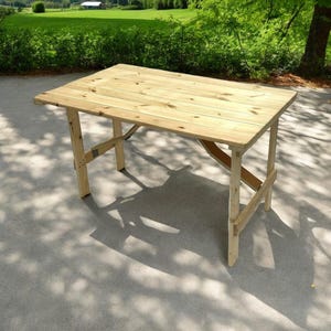 May include: A light wood folding table with a natural finish. The table is made of planks of wood and has a simple, rustic design.
