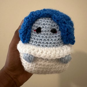 May include: A crocheted plush toy with a blue head and white body. The toy has black eyes and a red mouth.