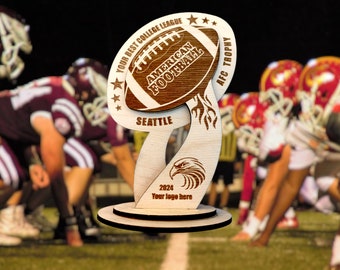 Könnte beinhalten: Eine Holz-Trophäe in Form eines Fußballs mit den Worten "Your Best College League", "American Football", "Seattle", "AFC Trophy" und "2024 Your logo here" eingraviert. Die Trophäe steht vor einem verschwommenen Hintergrund von Footballspielern.