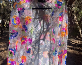May include: A sheer, open-front long-sleeve cardigan featuring vibrant, multi-colored floral embroidery and dense sequin embellishments in shades of neon pink, bright blue, orange, and green on a lightweight, translucent white mesh fabric.