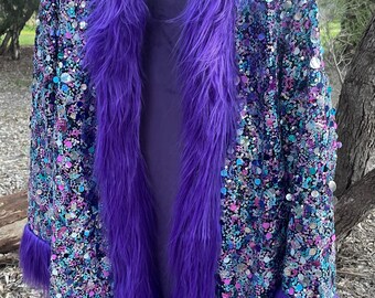 May include: A purple sequined jacket with a faux fur collar and cuffs. The jacket is covered in a mix of colorful sequins and has a long, open design. The faux fur is a vibrant purple color.