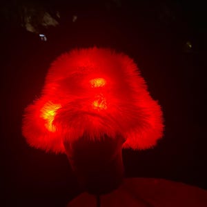 May include: A red, fluffy hat with illuminated sections. The hat is the primary focus, glowing brightly against a dark background. The hat's texture appears soft and plush, with a vibrant, eye-catching colour.