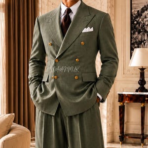 Op de afbeelding: Een saliegroen dubbelbreasted pak met gouden knopen, een wit pochet en een bruine stropdas. Het pak wordt gecombineerd met een broek met wijde pijpen. De afbeelding bevat de tekst "MAANMUK Dress to Succeed".