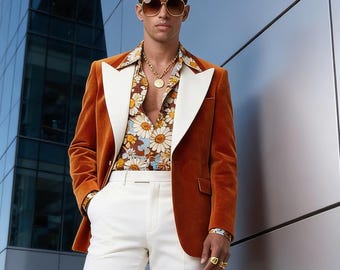 May include: A man wearing a rust-colored velvet blazer with white lapels, a floral print shirt, and white flared pants. The outfit is accessorized with gold jewelry and sunglasses. The logo "MAANMUK Dress to Succeed" is visible.