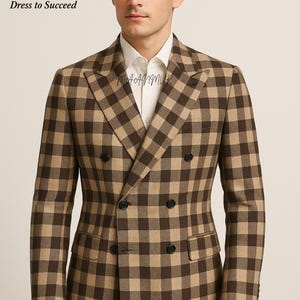 Può includere: Giacca da abito a quadri marrone e beige a doppio petto con bottoni neri. La giacca è indossata sopra una camicia bianca. Il marchio "MAANMUK Dress to Succeed" è visibile in alto a sinistra.