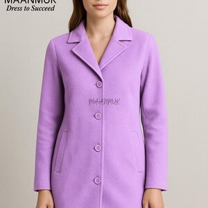 May include: A lavender-colored coat with a notched collar and three buttons down the front. The coat has two front pockets and the brand name "MAANMUK Dress to Succeed" is visible in the upper left corner. The brand name "MAANMUK" is also printed on the coat.