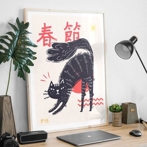 Puede incluir: Una impresi&oacute;n enmarcada de un gato negro con un sol rojo detr&aacute;s. El gato est&aacute; arqueado con la espalda hacia el espectador. La impresi&oacute;n tiene los caracteres chinos "春節" (Festival de Primavera) y una peque&ntilde;a estrella en la esquina superior derecha.